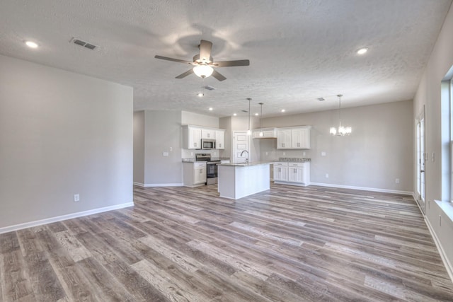 kitchen featuring a textured ceiling, a center island with sink, pendant lighting, stainless steel appliances, and white cabinets