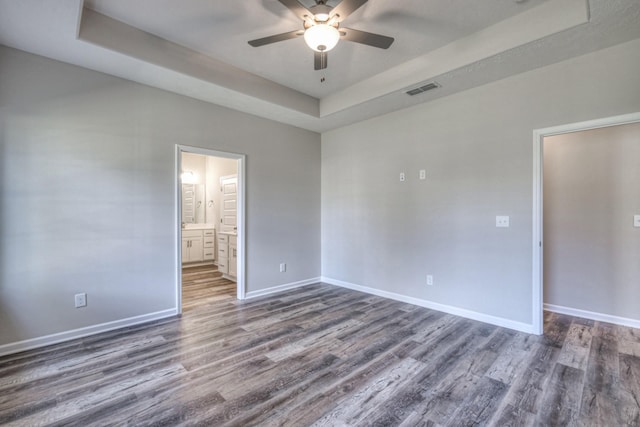 empty room with a raised ceiling, dark hardwood / wood-style floors, and ceiling fan