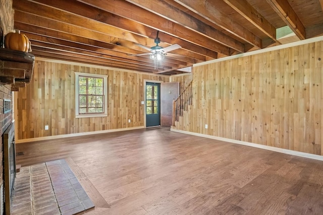 unfurnished room featuring beamed ceiling, wooden walls, a brick fireplace, and wood-type flooring