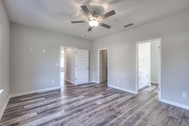 unfurnished bedroom with hardwood / wood-style floors, a walk in closet, ceiling fan, ensuite bath, and a closet