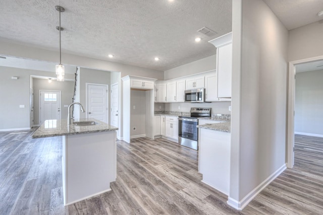 kitchen featuring sink, appliances with stainless steel finishes, white cabinetry, light stone counters, and decorative light fixtures