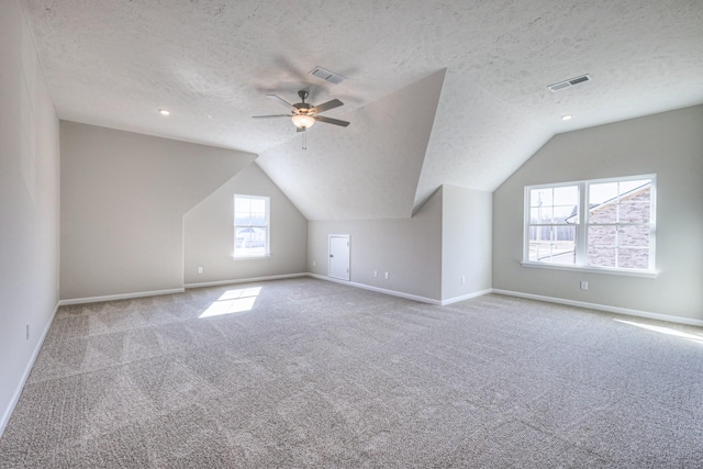 bonus room with ceiling fan, vaulted ceiling, light colored carpet, and a textured ceiling