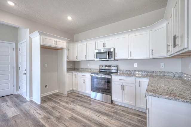 kitchen featuring light hardwood / wood-style flooring, white cabinetry, stainless steel appliances, light stone counters, and a textured ceiling