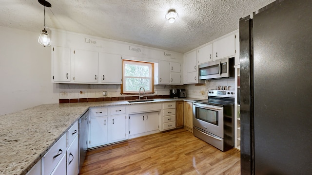 kitchen featuring appliances with stainless steel finishes, sink, decorative light fixtures, white cabinets, and light hardwood / wood-style flooring