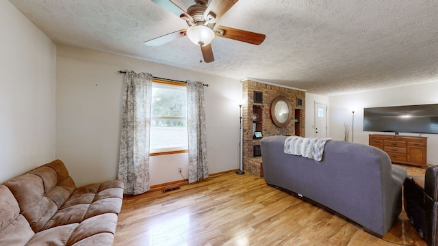 living room with light hardwood / wood-style flooring, a textured ceiling, a brick fireplace, and ceiling fan