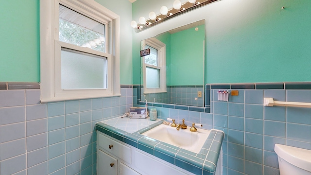 bathroom with toilet, tile walls, vanity, and plenty of natural light