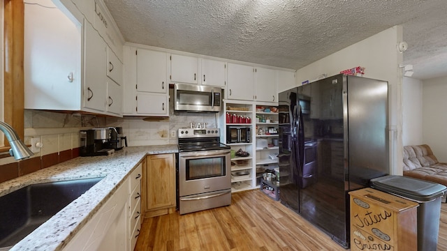 kitchen featuring light stone countertops, sink, black appliances, white cabinetry, and light hardwood / wood-style flooring