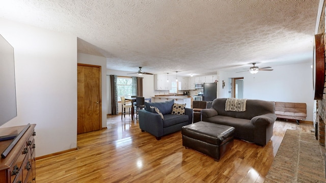 living room with light hardwood / wood-style flooring, a textured ceiling, and ceiling fan