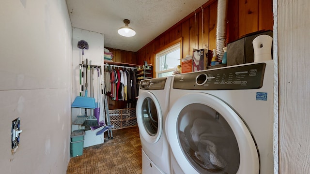 washroom with a textured ceiling, washing machine and clothes dryer, and wood walls