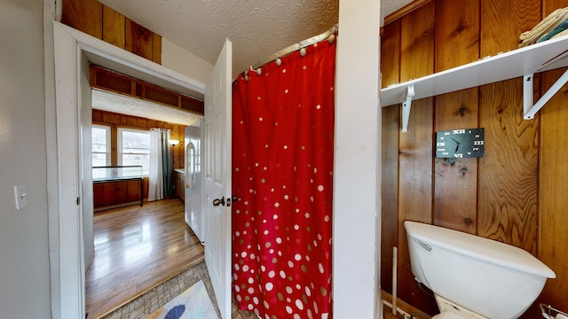 bathroom featuring toilet, a textured ceiling, wooden walls, and wood-type flooring