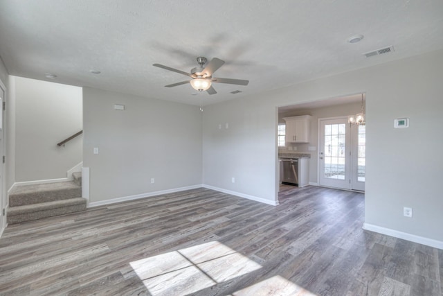 unfurnished living room with ceiling fan with notable chandelier, a textured ceiling, and light wood-type flooring