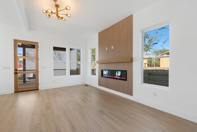 unfurnished living room with a chandelier, a large fireplace, and light wood-type flooring