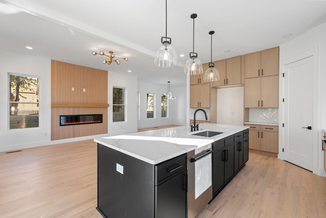 kitchen featuring a healthy amount of sunlight, a kitchen island with sink, sink, and hanging light fixtures