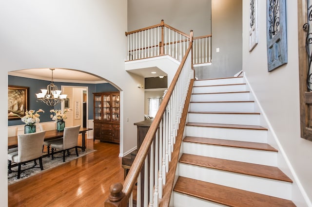 staircase with hardwood / wood-style floors, a notable chandelier, crown molding, and a high ceiling