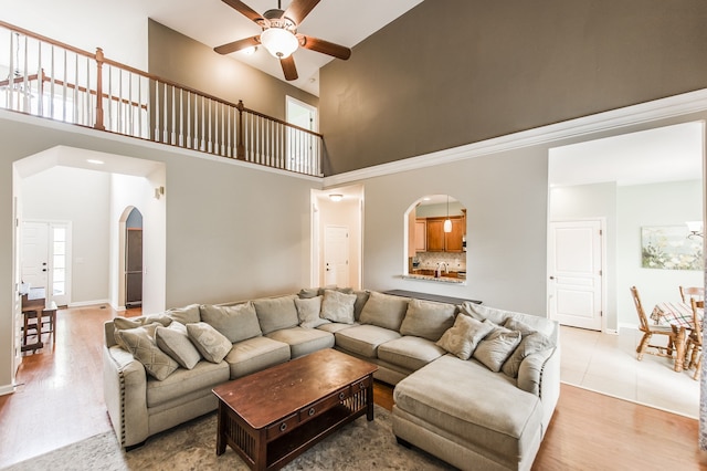 living room featuring plenty of natural light, ceiling fan, a towering ceiling, and light wood-type flooring