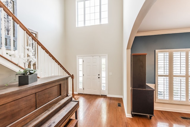 foyer with ornamental molding, a high ceiling, and light hardwood / wood-style floors