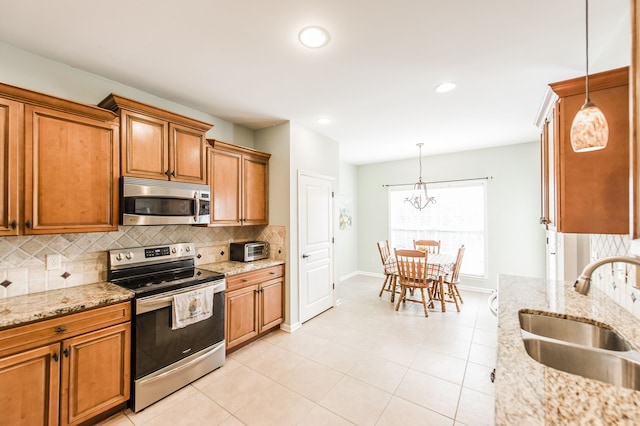 kitchen featuring tasteful backsplash, light stone countertops, sink, appliances with stainless steel finishes, and decorative light fixtures