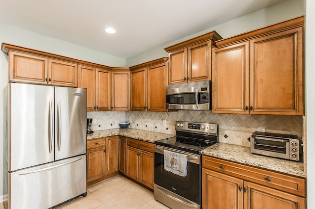 kitchen with light stone countertops, stainless steel appliances, backsplash, and light tile patterned floors