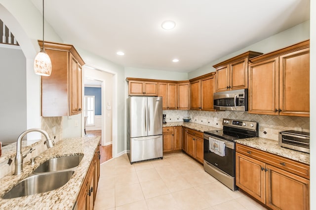 kitchen featuring hanging light fixtures, backsplash, sink, appliances with stainless steel finishes, and light stone counters