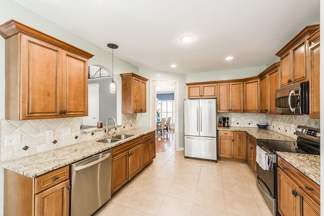 kitchen with light stone counters, appliances with stainless steel finishes, sink, and pendant lighting