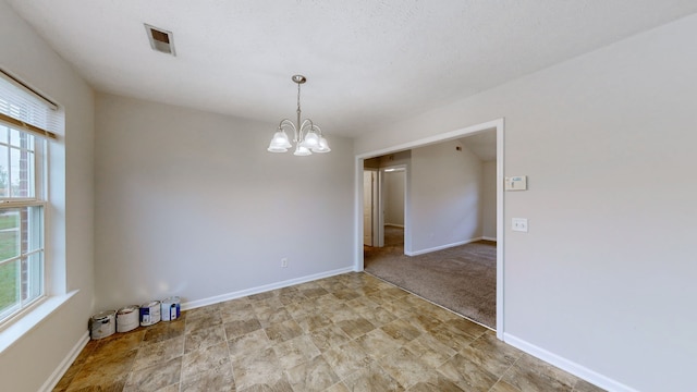 unfurnished room with a textured ceiling, a healthy amount of sunlight, light carpet, and a chandelier