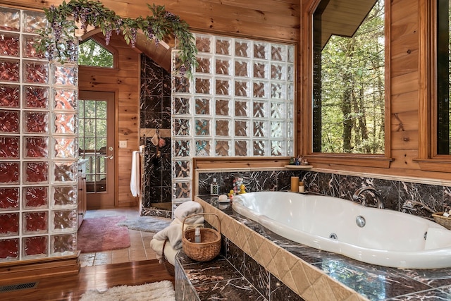 bathroom featuring a bathing tub, vaulted ceiling, hardwood / wood-style flooring, and wood walls