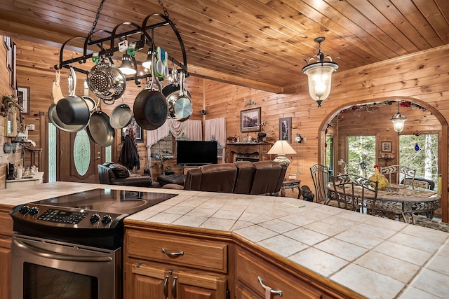 kitchen with wood ceiling, tile countertops, wooden walls, stainless steel electric stove, and pendant lighting