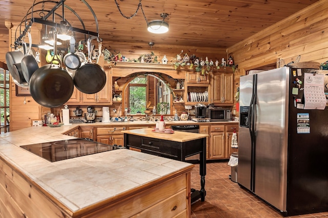 kitchen featuring tile countertops, black appliances, a center island, and wood walls