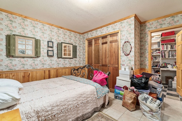 bedroom with a closet, ornamental molding, light tile patterned flooring, a textured ceiling, and wood walls