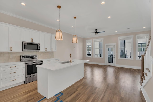 kitchen featuring a kitchen island with sink, white cabinets, sink, decorative light fixtures, and stainless steel appliances