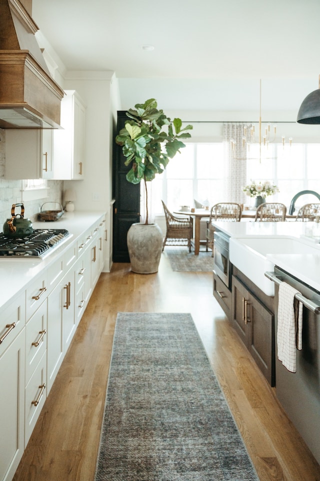 kitchen with light wood-type flooring, white cabinetry, stainless steel appliances, decorative light fixtures, and custom range hood