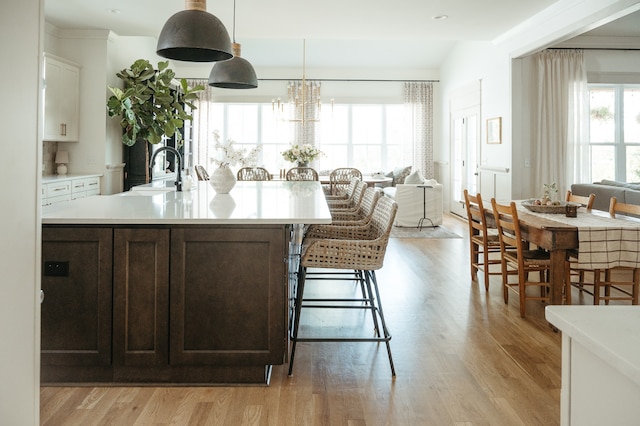 kitchen featuring light hardwood / wood-style flooring, a center island with sink, sink, decorative light fixtures, and white cabinetry