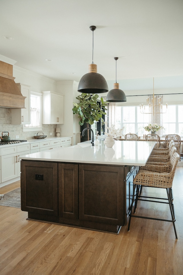 kitchen featuring light wood-type flooring, a large island with sink, plenty of natural light, and hanging light fixtures