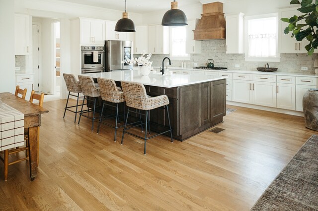 kitchen with appliances with stainless steel finishes, hanging light fixtures, light wood-type flooring, and plenty of natural light