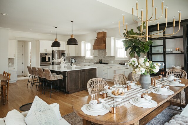 kitchen featuring a kitchen island with sink, hardwood / wood-style flooring, stainless steel fridge, decorative light fixtures, and white cabinetry