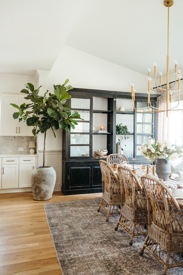 dining space with light hardwood / wood-style floors, an inviting chandelier, and vaulted ceiling