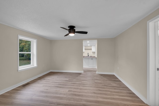 empty room with ceiling fan, crown molding, sink, and light wood-type flooring