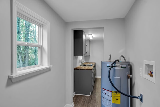 laundry area featuring hookup for a washing machine, sink, dark wood-type flooring, electric water heater, and cabinets