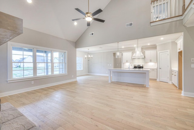 unfurnished living room featuring ceiling fan with notable chandelier, high vaulted ceiling, sink, and light wood-type flooring