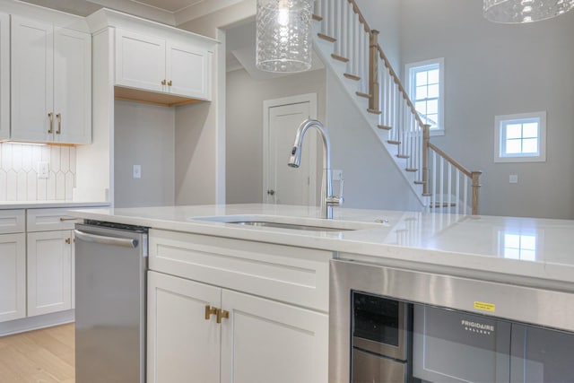 kitchen featuring pendant lighting, stainless steel dishwasher, sink, and white cabinets