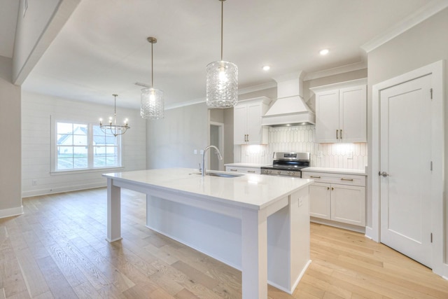 kitchen featuring sink, stainless steel range, an island with sink, custom range hood, and pendant lighting