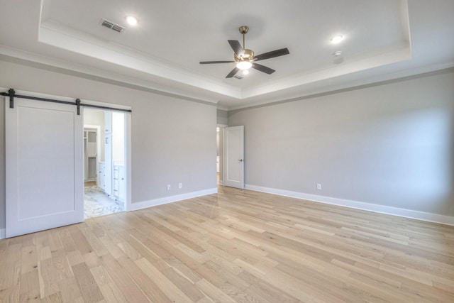 unfurnished bedroom with ornamental molding, light hardwood / wood-style floors, a raised ceiling, and a barn door