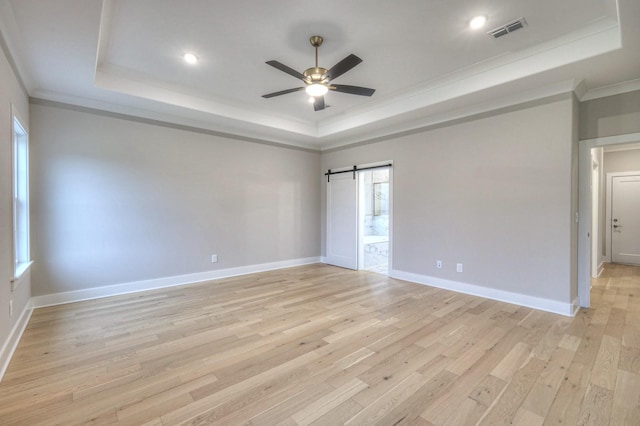 empty room with crown molding, a barn door, light wood-type flooring, and a tray ceiling