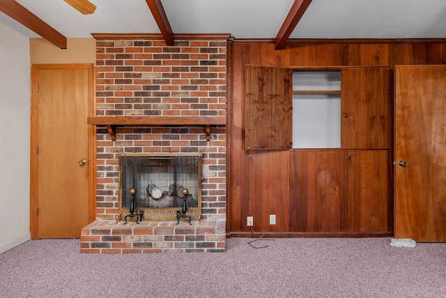 unfurnished living room with beam ceiling, light carpet, a brick fireplace, and wooden walls