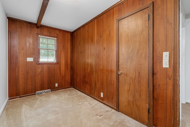 unfurnished bedroom with beam ceiling, light carpet, and wood walls