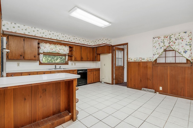 kitchen with sink, wooden walls, dishwasher, and light tile patterned floors