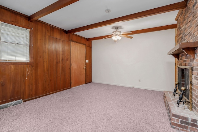 unfurnished living room with beamed ceiling, wooden walls, light carpet, a fireplace, and ceiling fan