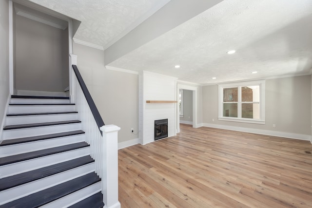 unfurnished living room featuring light hardwood / wood-style floors, crown molding, a textured ceiling, and a fireplace