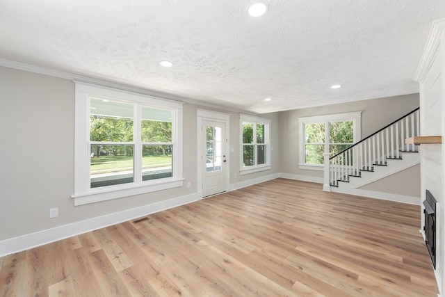 unfurnished living room featuring a textured ceiling, a wealth of natural light, light wood-type flooring, and ornamental molding