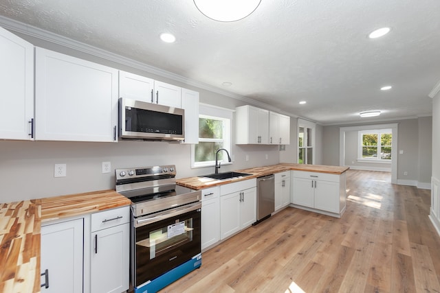 kitchen with appliances with stainless steel finishes, white cabinetry, light wood-type flooring, wooden counters, and sink